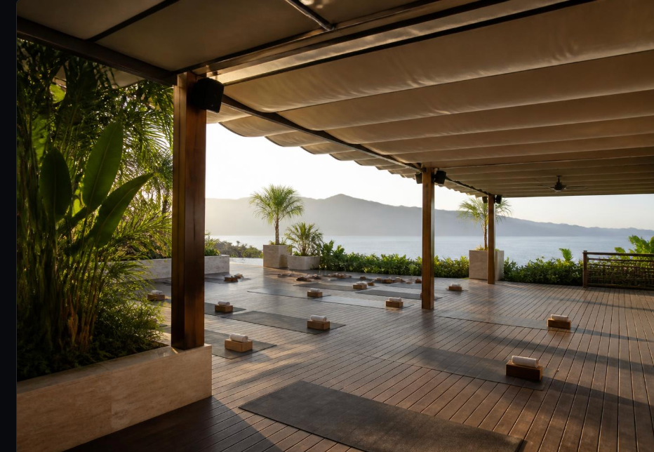 Covered outdoor timber deck with yoga mats and sea view at golden hour
